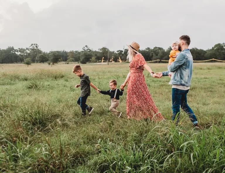 Une famille se promenant dans un champ verdoyant, main dans la main, sous un ciel nuageux.