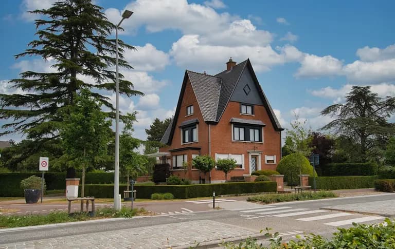Maison familiale en briques avec un jardin verdoyant, située dans un quartier résidentiel calme de Visé, sous un ciel bleu.